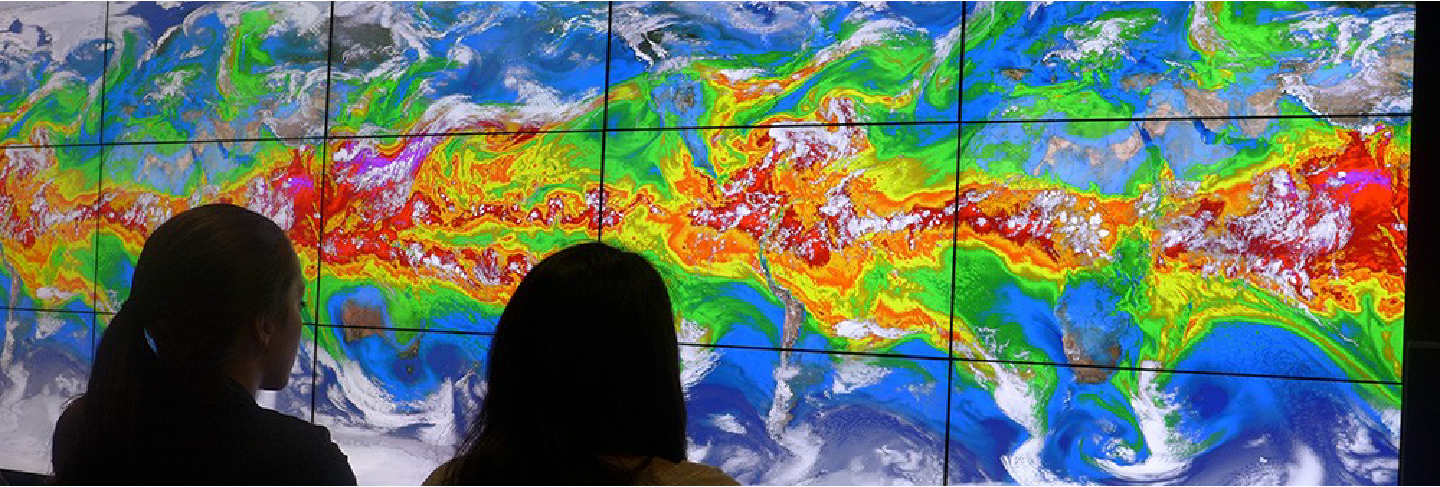 Two women watching a large heat map with many swirling colors.
