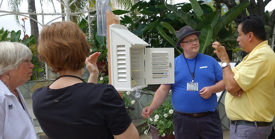 Four adults standing around scientific equipment, explaining it to each other, surrounded by plants.
